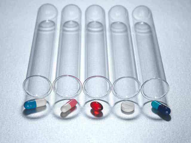 Four test tubes lying lengthwise with assorted pills placed at the outside of the openings