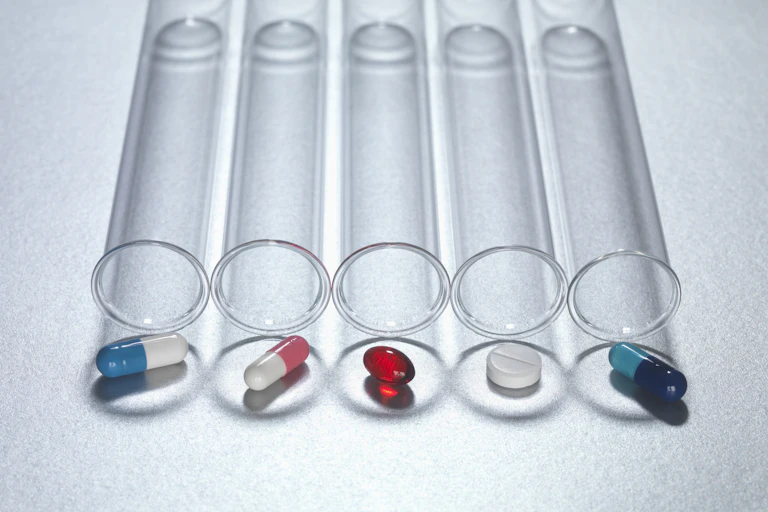 Four test tubes lying lengthwise with assorted pills placed at the outside of the openings