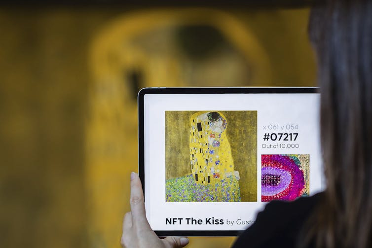 over-the-shoulder view of a person holding a tablet displaying an image of a painting