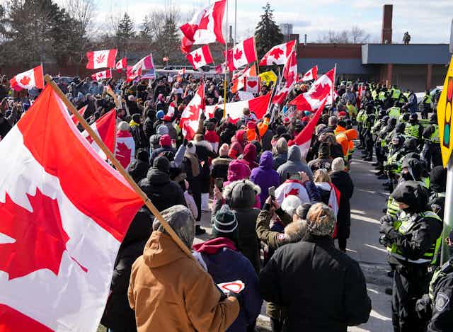 A line of police officials look at a group of protesters with Canadian flags 