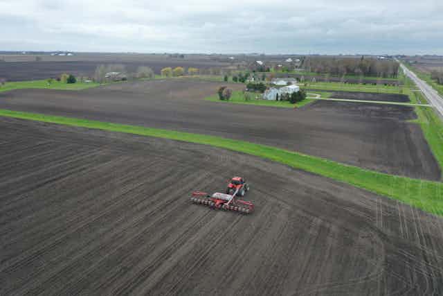 Aerial view of a tractor pulling a seed corn planter across a large field.