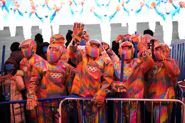A group of people in colourful snow suits and helmets waving.