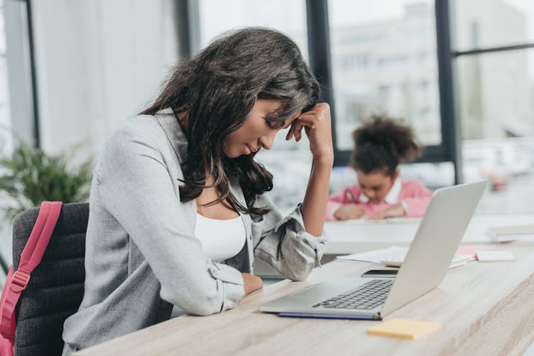 A woman sits at her laptop with her hand on hear head