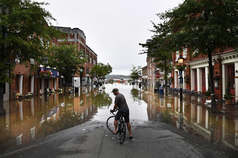 A man on a bicycle looks at flood water covering most of a downtown street.