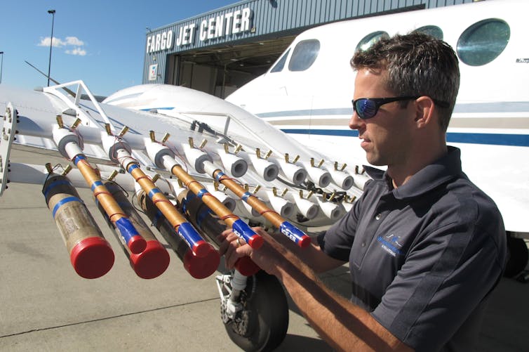 A man attaches a row of canisters to an airplane wing.