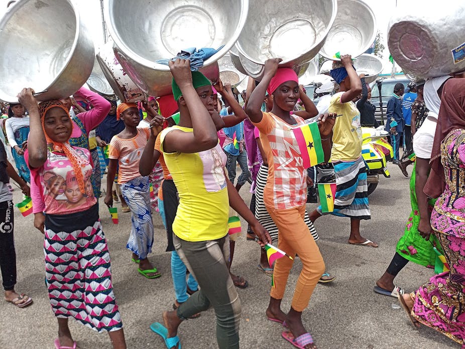 A group of young Ghanaian women carrying pans on their heads as they walk