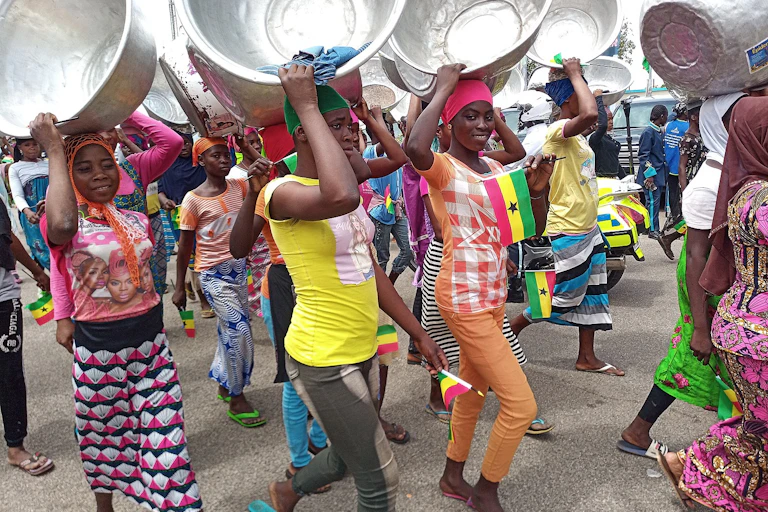 A group of young Ghanaian women carrying pans on their heads as they walk
