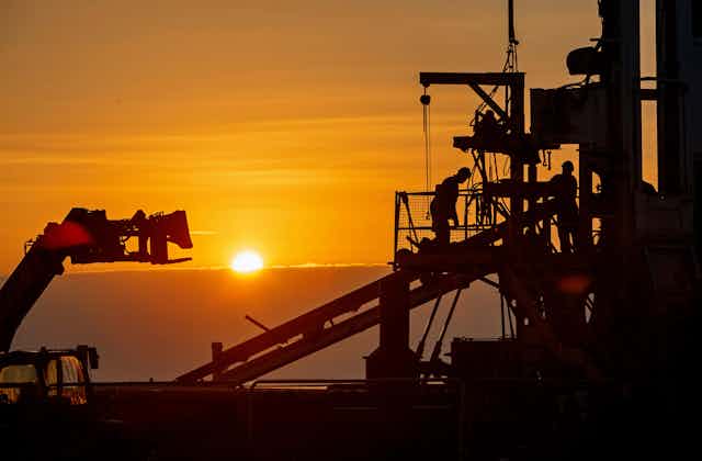 Workers on a drill rig silhouetted at sunset.