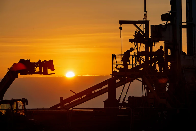Workers on a drill rig silhouetted at sunset.