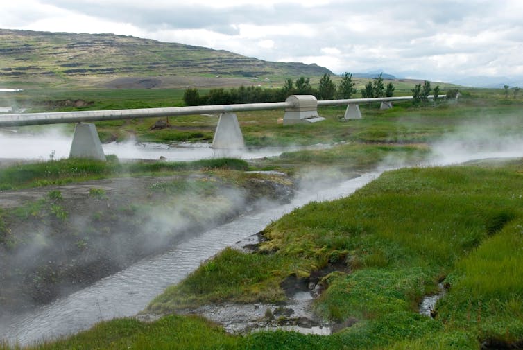 A pipeline runs through a steaming, green landscape.