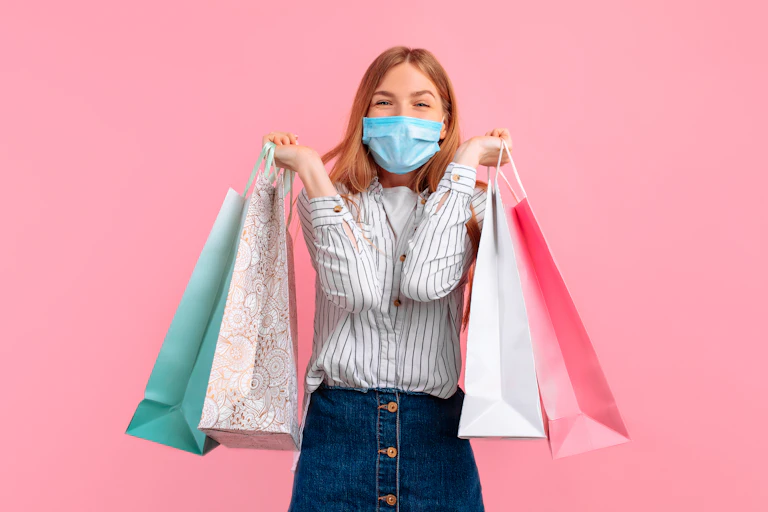 Smiling woman in face mask holds several shopping bags.