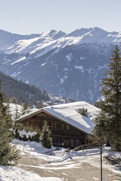 Aerial view of a large chalet with snow-covered Swiss mountains in the background