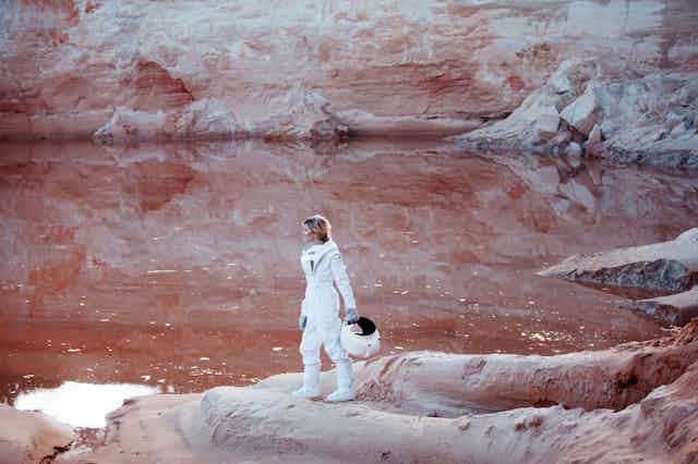 Woman in space suit with helmet off in red landscape