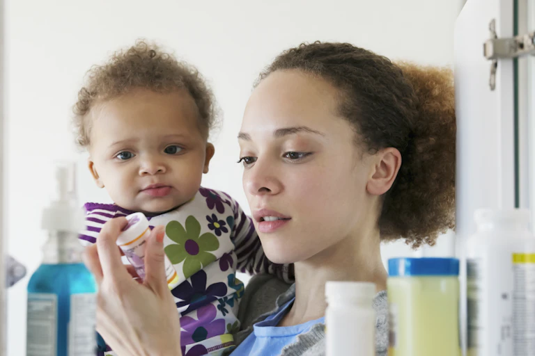 A woman holding a baby looks at a bottle of prescription pills.
