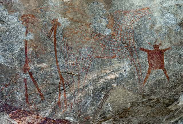 Rock wall showing ancient painting of people, giraffe
