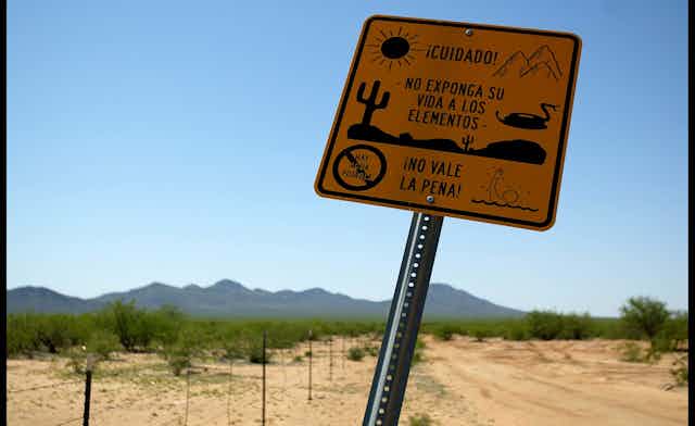 A yellow sign says "cuidado!" -- meaning caution in Spanish. The backdrop of a desert on a clear blue day is behind the sign.