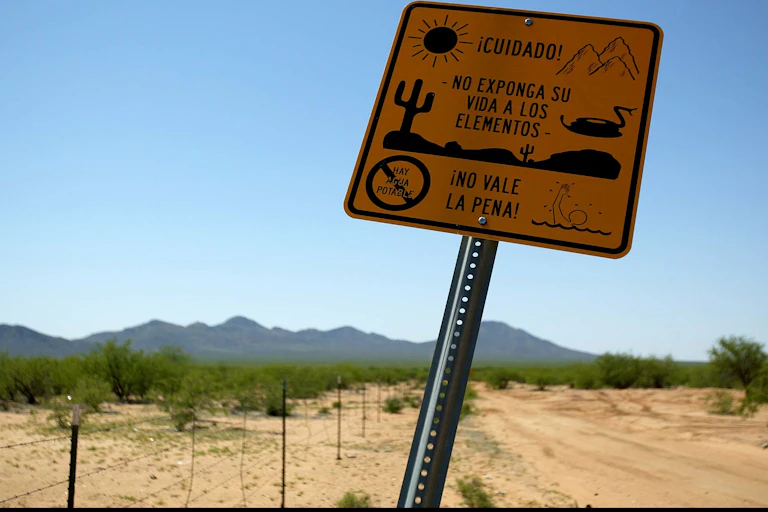 A yellow sign says "cuidado!" -- meaning caution in Spanish. The backdrop of a desert on a clear blue day is behind the sign.
