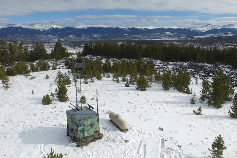 A box with a pipe above it for releasing chemicals on a snowy hilltop.