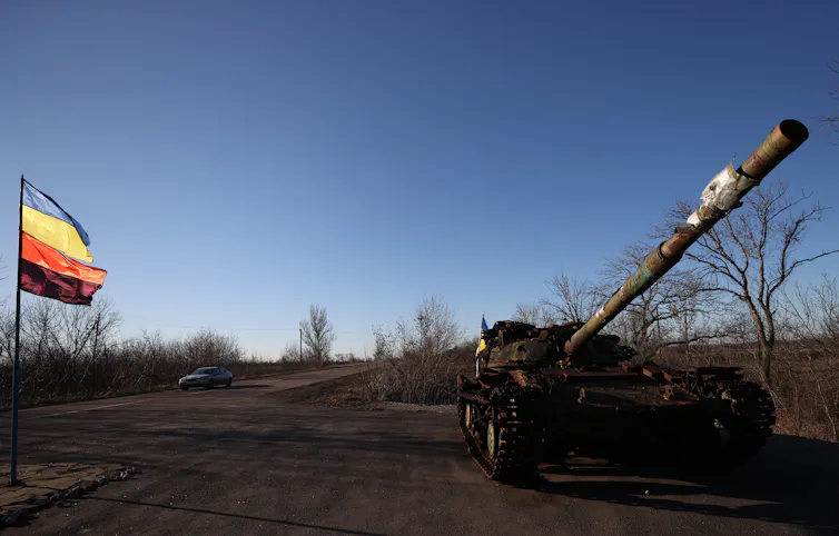 A tank sits by the side of an open road with a flag visible.