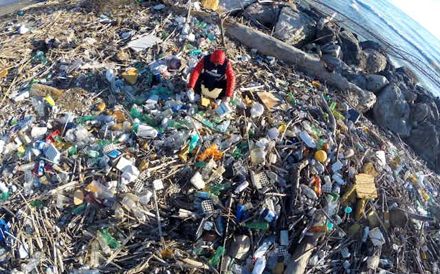 A person searching through piles of plastics on a river bank