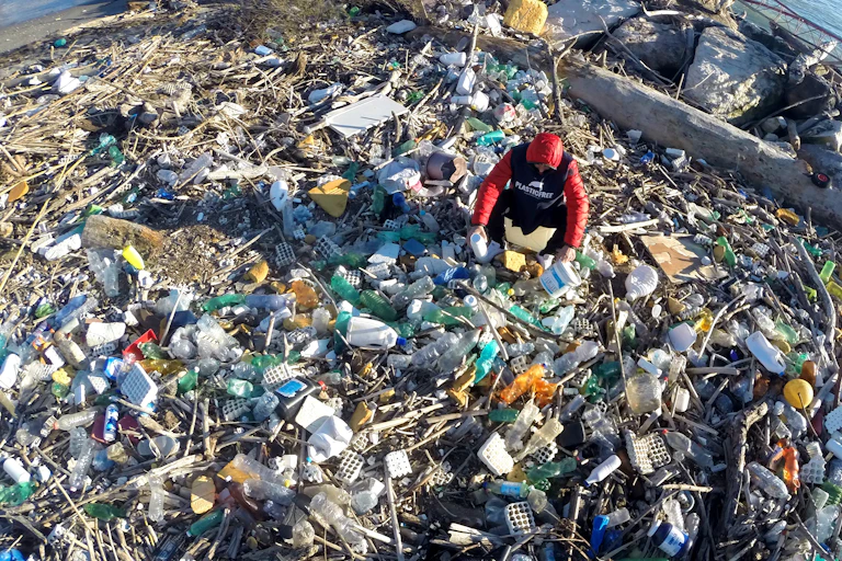 A person searching through piles of plastics on a river bank
