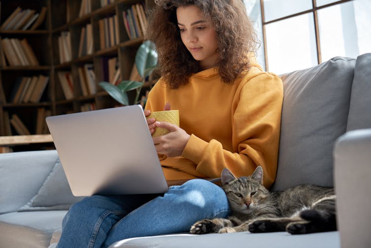 Young female sitting on sofa with a cat leaning against her