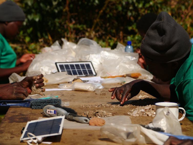 Workers at a table sort tiny archaeological items by hand