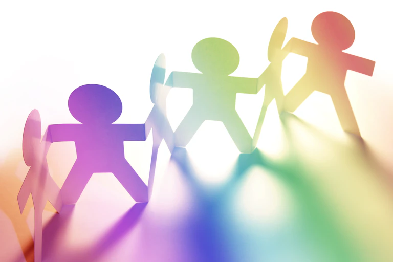 A paper chain of six people shaped figures, cast in a rainbow of light