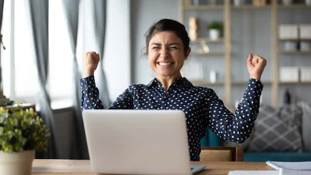 Woman celebrates while sitting at laptop.