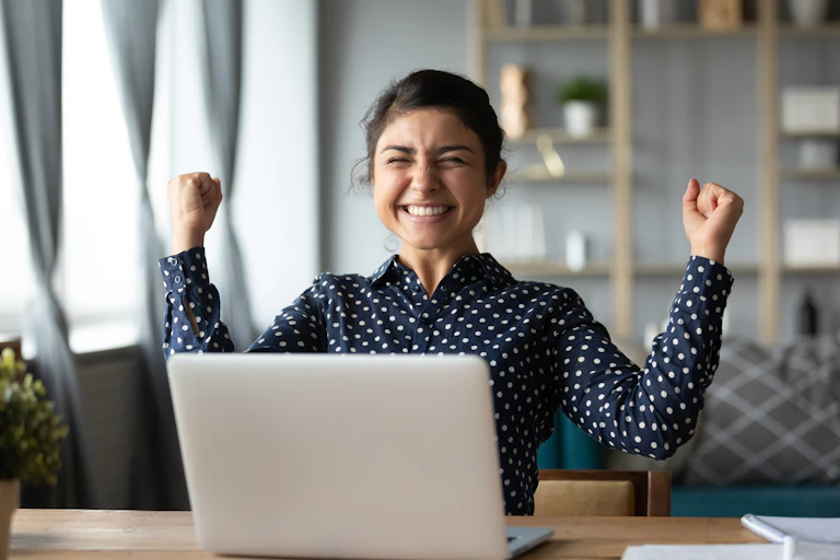 Woman celebrates while sitting at laptop.