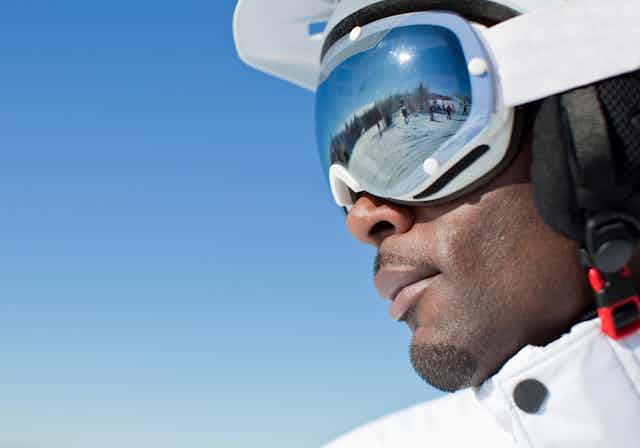 A Black skier with other skiers reflected in his goggles.