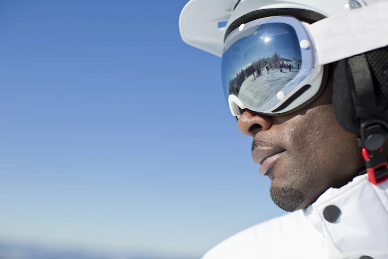 A Black skier with other skiers reflected in his goggles.