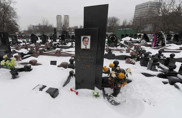 Flowers are placed by an obelisk memorial bearing a photo of Sergei Magnitsky in a snowy cemetery.