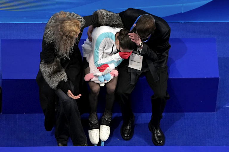 A girl sits with her hands over her face as two people comfort her from either side.