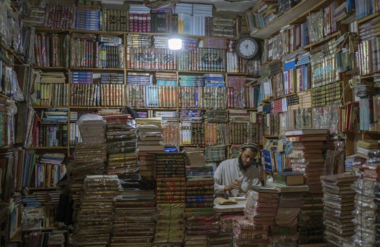 A man is seen surrounded by towering books in a bookshop.