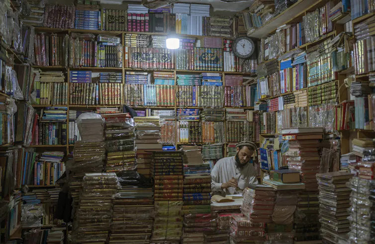 A man is seen surrounded by towering books in a bookshop.