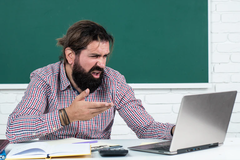 Bearded man gestures in dismay as he reads from his laptop