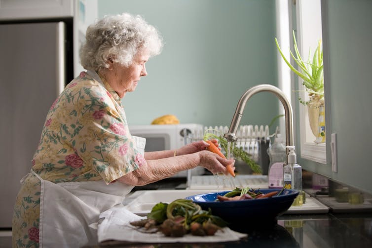 older woman washes hands in kitchen