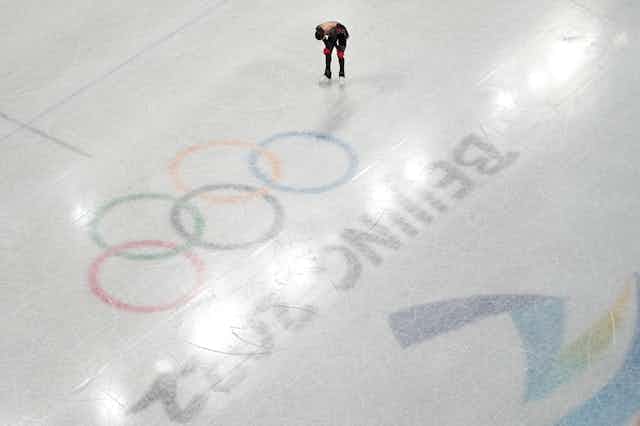 Valieva puts her hands on her thighs in a photo shot from above ice level that shows the Olympic rings on the ice