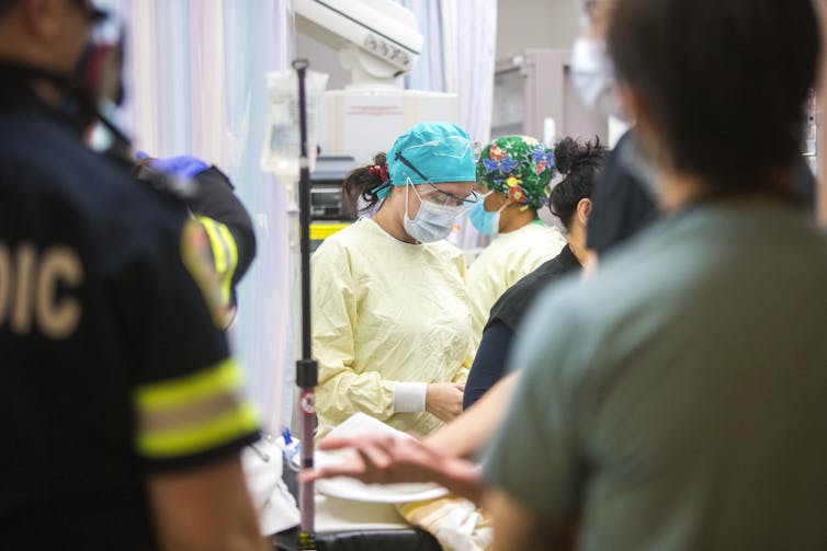 Medical staff wearing gowns, caps and face masks with two figures in the foreground seen from behind