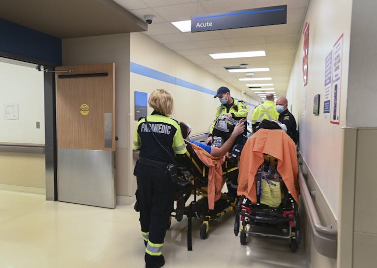 Paramedics wheeling a patient on a gurney draped in orange in a crowded hospital corridor