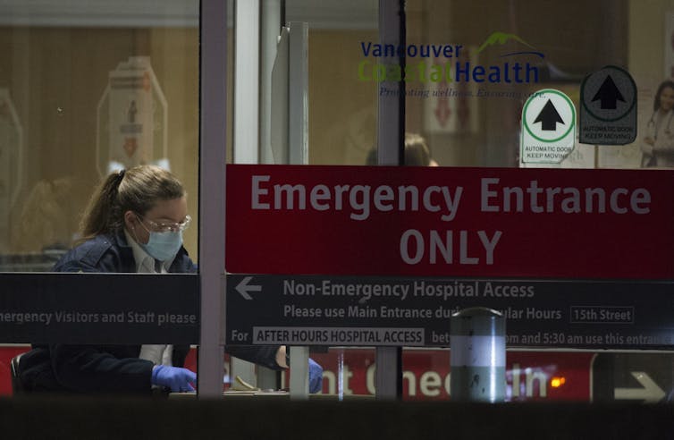 A hospital worker is seen through the glass entrance doors of an emergency department