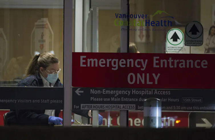 A hospital worker is seen through the glass entrance doors of an emergency department