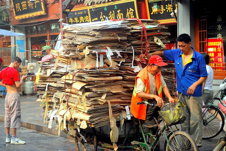 A person rides a bicycle towing cardboard