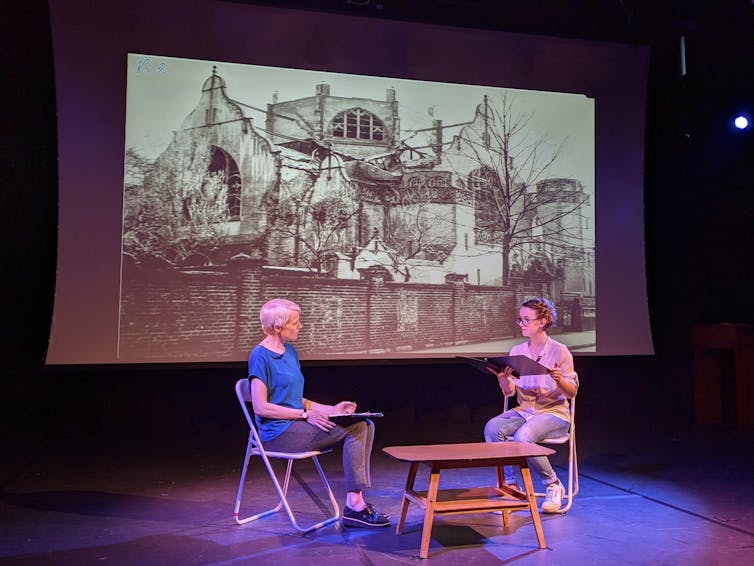 Two woman on stage beneath a banner showing a picture of a synogogue.