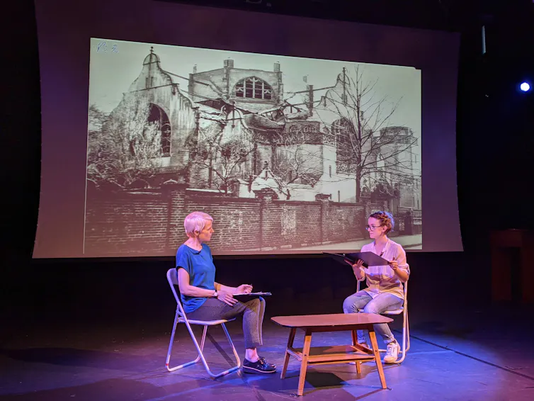 Two woman on stage beneath a banner showing a picture of a synogogue.