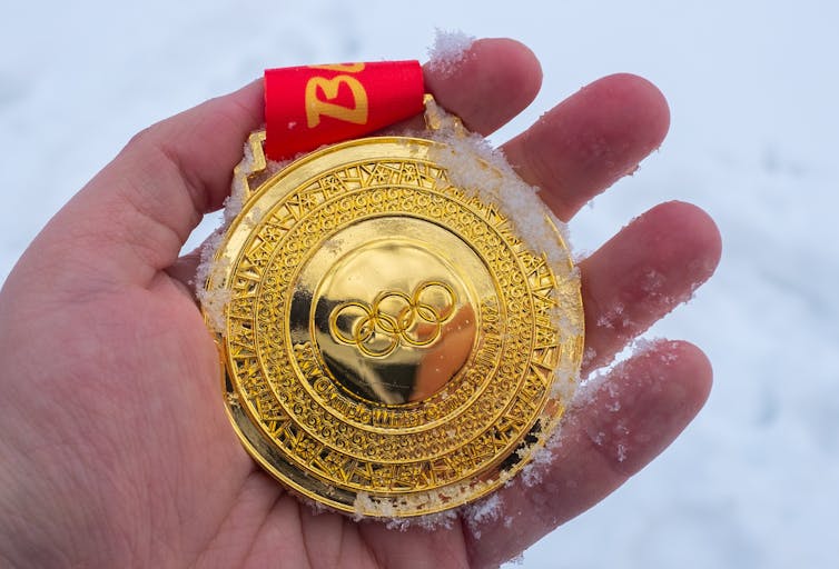 A person holds a gold medal from the Beijing 2022 Winter Olympics in their hand.