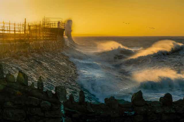 Large waves break on a pier at sunrise.