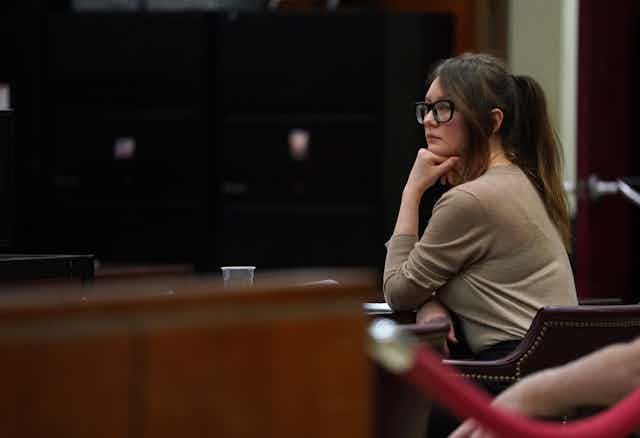 Woman with glasses rests her chin on her fist in a courtroom.