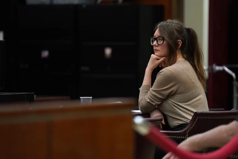 Woman with glasses rests her chin on her fist in a courtroom.